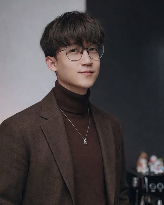 Huy Nguyen mặc áo khoác nâu, mỉm cười trước ống kính.